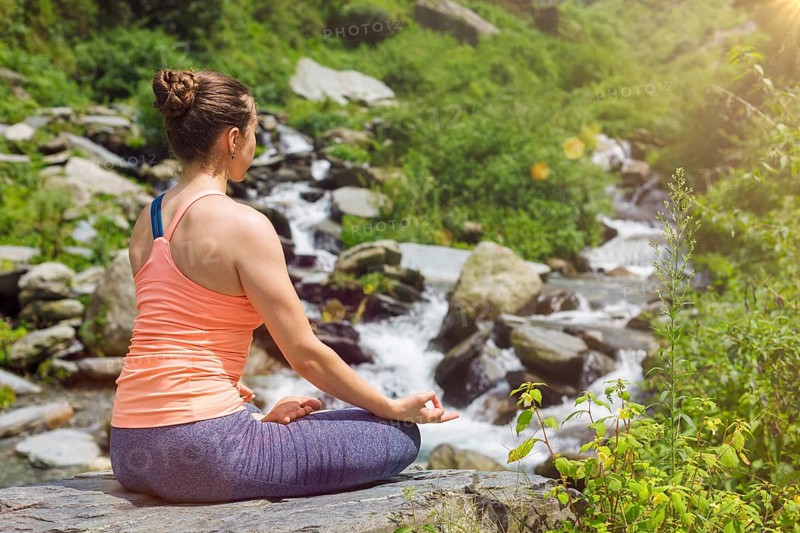 Woman in Hatha yoga asana Padmasana outdoors at tropical waterfall