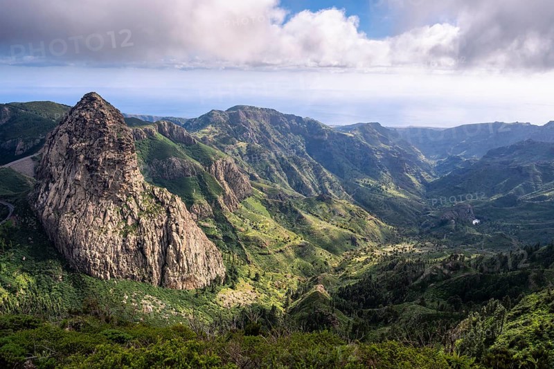 View of the Roque de Agando rock tower from the Mirador del Morro de Agando. To the right is the Barranco de Benchijigua gorge. During the day, sun and clouds, good weather. Monumento Natural de Los Roques, Reserva Natural Integral Benchijigua, La Gomera, Canary Islands, Spain, Europe