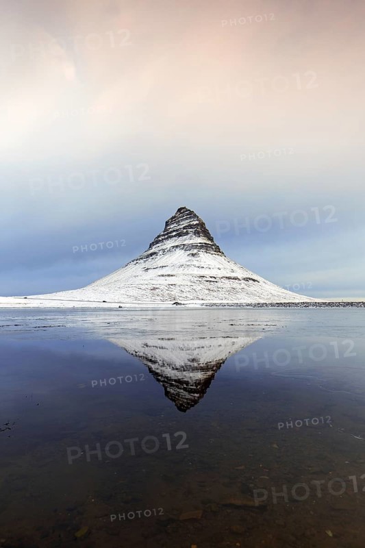 Kirkjufell, nunatak hill covered in snow reflected in water of fjord on the Snæfellsnes peninsula in winter, most photographed mountain in Iceland
