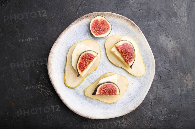 Summer appetizer with pear, cottage cheese, figs and honey on ceramic plate on a black concrete background. Top view, flat lay, close up