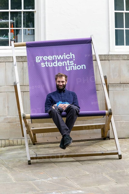Young man sitting in giant deckchair outside the Students' Union, Greenwich, London SE10, England, UK