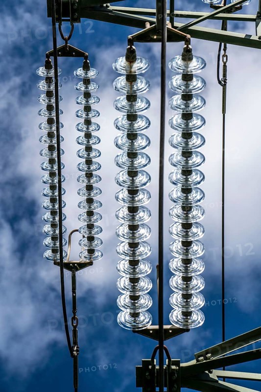 Insulators made of glass on a high-voltage line, they hang on the pylons as a suspension device between the pylon and the live, non-insulated cable, extra-high voltage line, symbolic image energy