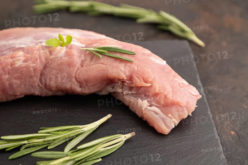 Raw pork meat with herbs and spices on slate cutting board on black concrete background. Side view, close up, selective focus