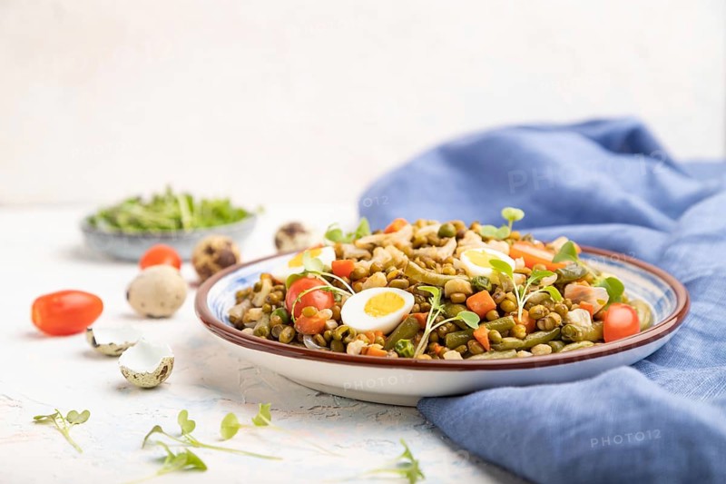 Mung bean porridge with quail eggs, tomatoes and microgreen sprouts on a white concrete background and blue textile. Side view, copy space, selective focus