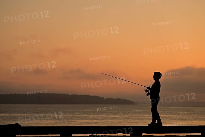 Boy at sunset standing on a pier and fishing for salmon, Vancouver Island