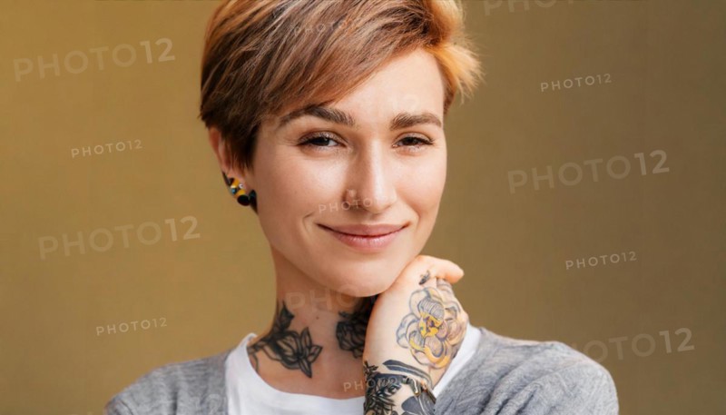 Portrait of a smiling woman with short hair and visible tattoos on a warm-coloured background, AI generated, AI generated