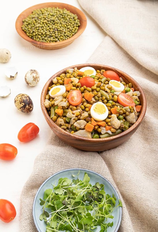 Mung bean porridge with quail eggs, tomatoes and microgreen sprouts on a white wooden background and linen textile. Side view, close up