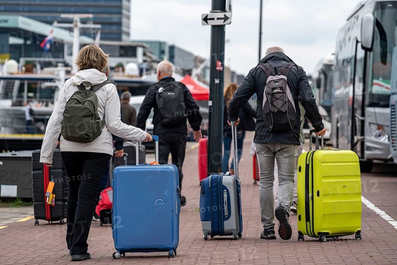 Travellers on their way to a river cruise ship at the quay of the Ij, transporting their luggage, wheeled suitcases, from the central station to the ship, Amsterdam, Netherlands