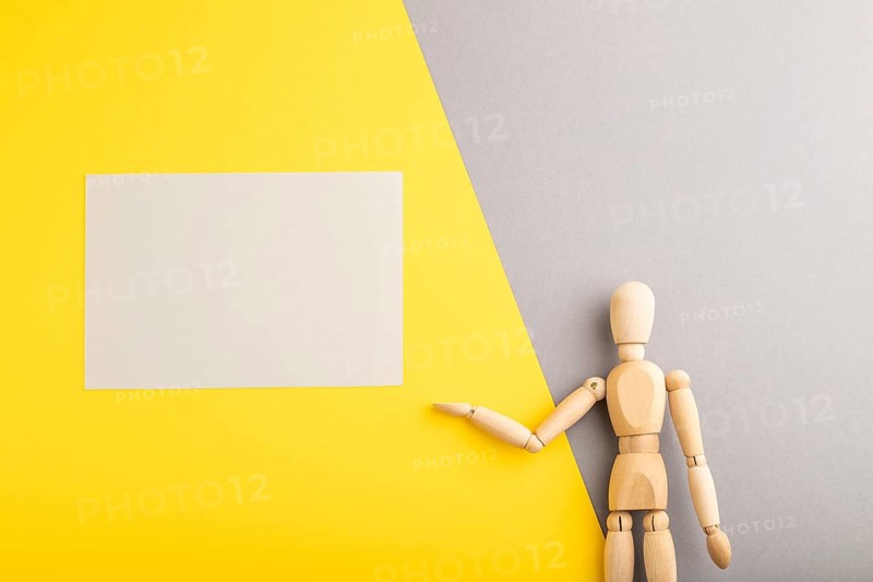 Wooden mannequin holding gray blank poster on gray and yellow pastel background. copy space, isolated, presentation concept, trendy colors