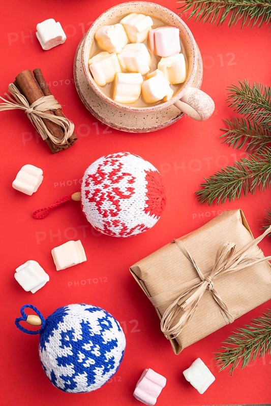 Christmas or New Year composition. Decorations, box, cinnamon, knitted balls, fir and spruce branches, cup of coffee, on a red paper background. Top view, close up, flat lay