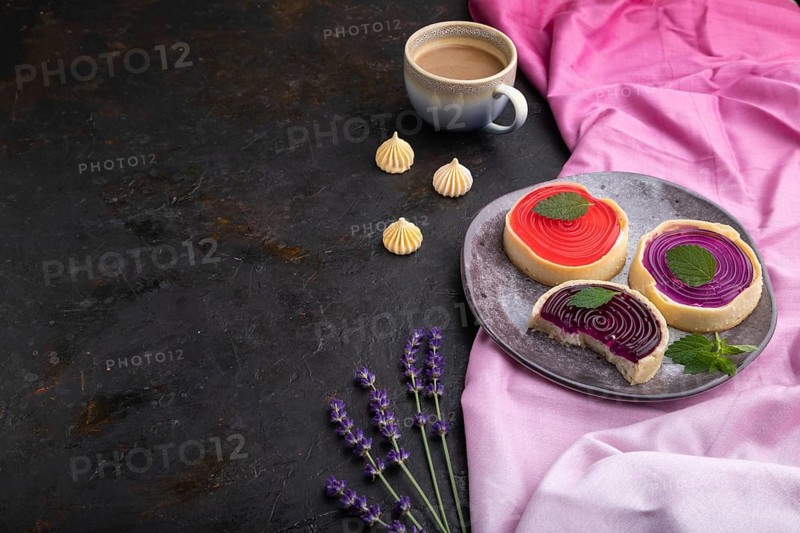 Sweet tartlets with jelly and milk cream with cup of coffee on a black concrete background and pink textile. Side view, copy space