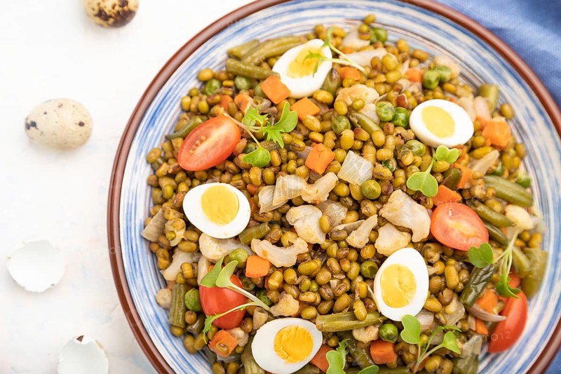 Mung bean porridge with quail eggs, tomatoes and microgreen sprouts on a white concrete background and blue textile. Top view, flat lay, close up