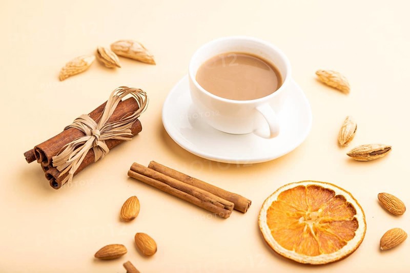 Composition with almonds, cinnamon and cup of coffee on orange pastel background. Blank, side view, still life, close up