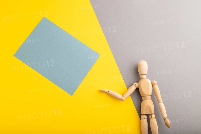 Wooden mannequin holding blue blank poster on gray and yellow pastel background. copy space, isolated, presentation concept, trendy colors