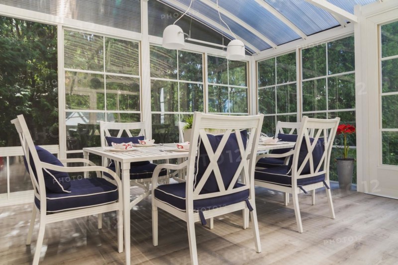 White dining table and armchairs with blue cushions in sunroom at back of luxurious residential home, Quebec, Canada, North America