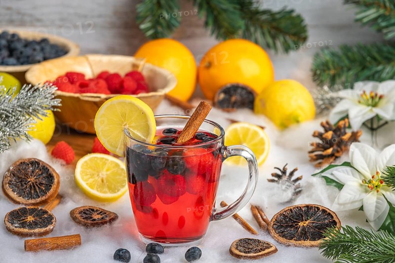 Punch in a glass cup, surrounded by oranges, lemons, raspberries and Christmas decorations