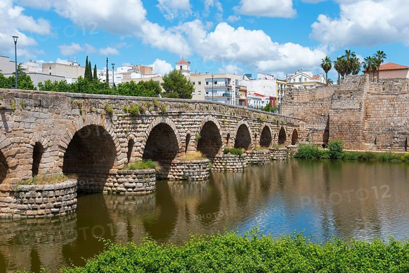 Historic stone bridge over a river with city wall in the background under a blue sky and summer atmosphere, Roman bridge, Puente Romano, arch bridge with wedge stone vault, Guadiana River, Mérida, Merida, Badajoz, Extremadura, Spain, Europe