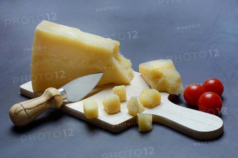 A piece of Parmesan cheese and chopped pieces of cheese on a wooden board