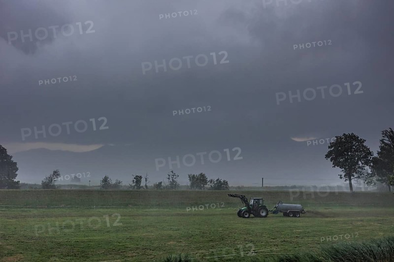 A farmer drives slurry onto a meadow with his tractor in the rain, storm, thunderstorm, Schlehdorf, Bavaria, Germany, Europe