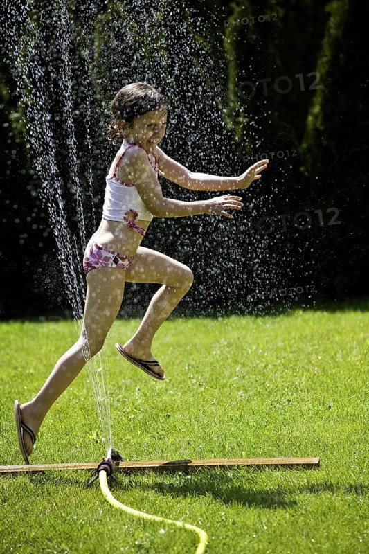 Young girl refreshing herself under a lawn sprinkler, Federal Republic of Germany