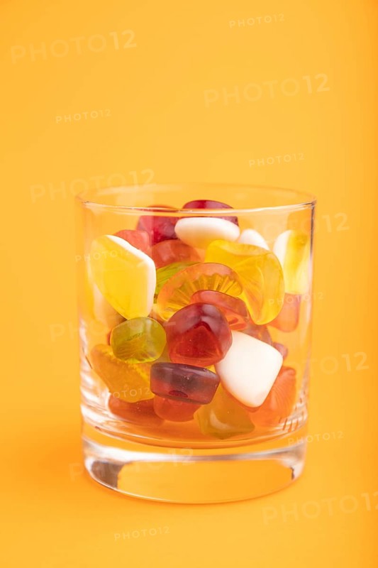 Various fruit jelly candies in drinking glass on orange pastel background. side view, close up