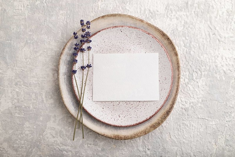 White paper invitation card, mockup with lavender on ceramic plate and gray concrete background. Blank, flat lay, top view, still life, copy space