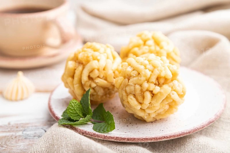 Traditional Tatar candy chak-chak made of dough and honey with cup of coffee on a white wooden background and linen textile. Side view, close up, selective focus