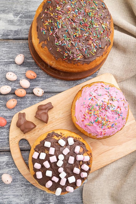 Homemade glazed and decorated easter pies with chocolate eggs and rabbits on a gray wooden background and linen textile. top view, flat lay, close up