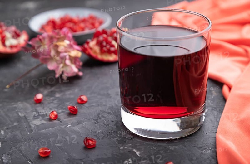 Glass of pomegranate juice on a black concrete background with red textile. Side view, close up, selective focus