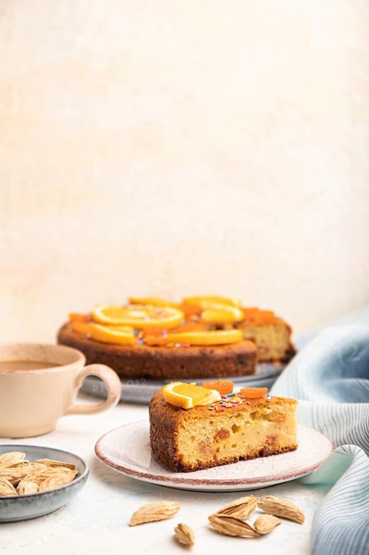Orange cake with almonds and a cup of coffee on a white concrete background and blue linen textile. Top view, copy space, selective focus