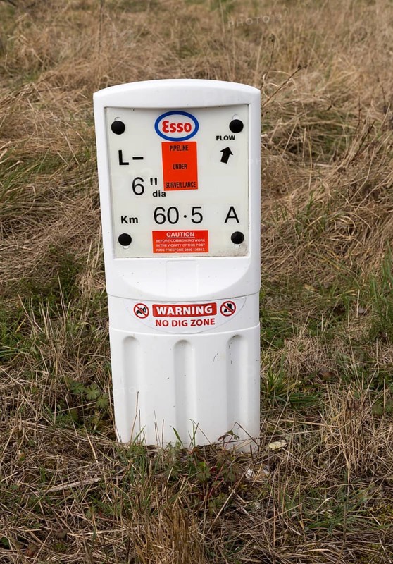 Close up of Esso gas pipeline under surveillance marker warning no dig zone, Salisbury Plain, Wiltshire, England, UK
