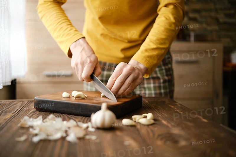 Unrecognizable man chopping garlic with knife on wooden cutting board