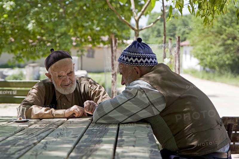 Two bearded elderly men wearing traditional taqiyah having a cup of tea on the main square of a small village in western Turkey