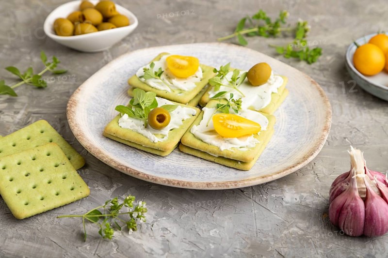 Green cracker sandwiches with cream cheese and cherry tomatoes on gray concrete background. side view, close up
