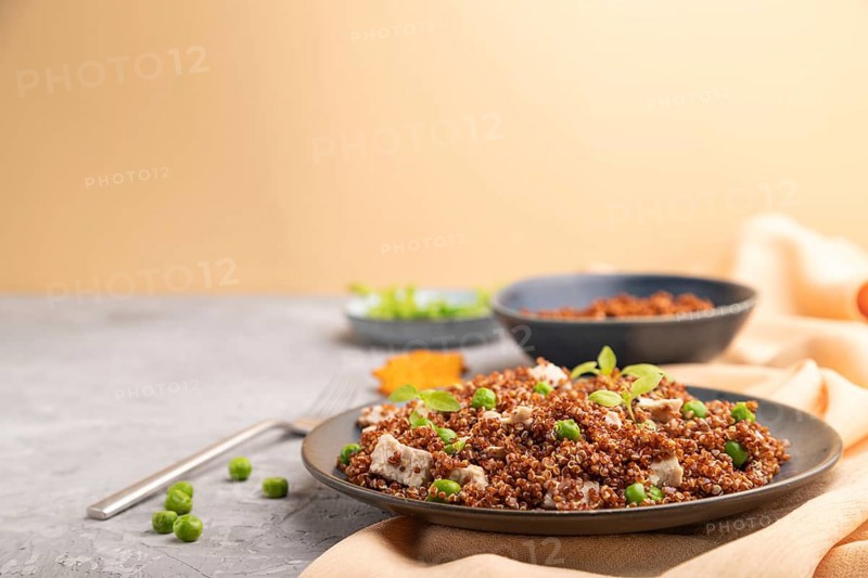 Quinoa porridge with green pea and chicken on ceramic plate on a gray concrete background and orange textile. Side view, copy space, selective focus