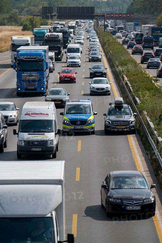 Police patrol car with flashing blue lights and siren working its way through a traffic jam on the A3 motorway, over 8 lanes, in both directions, between the Leverkusen motorway junction and the Cologne-Mülheim junction, looking south, Friday afternoon heavy traffic, delays due to the traffic jam, Leverkusen, North Rhine-Westphalia, Germany, Europe