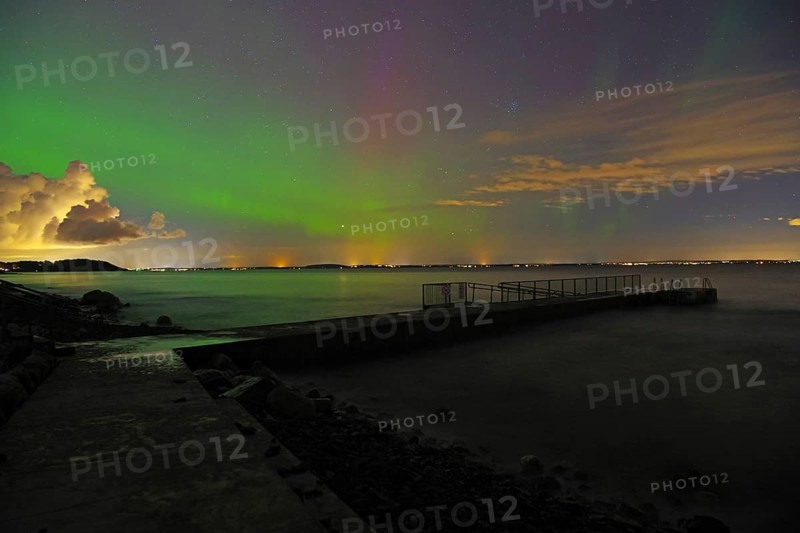 Northern Lights over a sea with distant city lights and partly cloudy sky, beach, Tönsberg, Oslofjord, Norway, Europe
