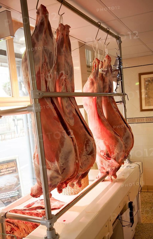 Whole lambs hanging from hooks inside a traditional butcher's shop, Marlborough, Wiltshire, England, UK