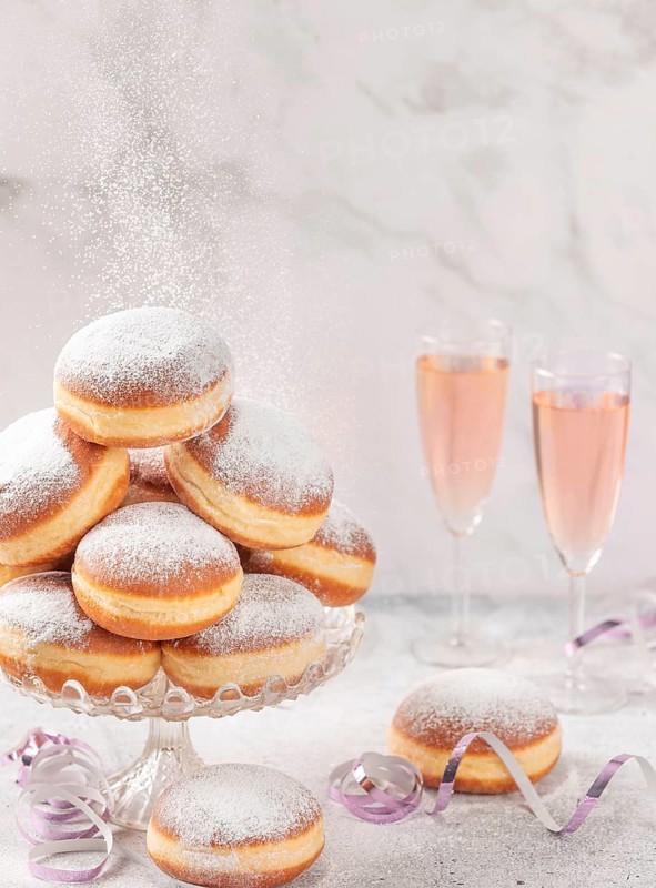 Doughnuts on a glass stand with rosé sparkling wine in the background and falling icing sugar