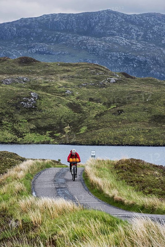 Lonely biker cycling through the Scottish Highlands on heavily laden touring bicycle along single track road in bad rainy weather, Scotland, UK