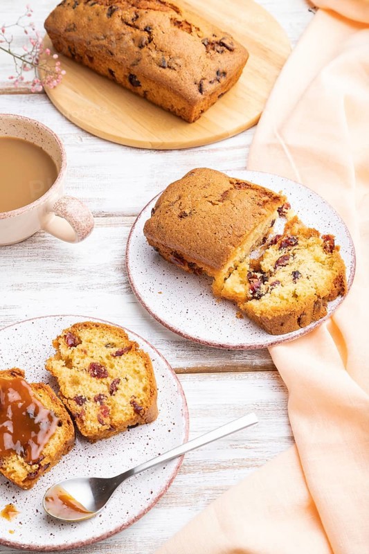 Homemade cake with raisins, almonds, soft caramel and a cup of coffee on a white wooden background and orange linen textile. Side view, close up
