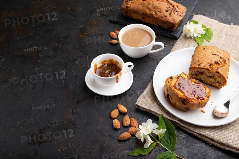 Homemade cake with raisins, almonds, soft caramel and a cup of coffee on a black concrete background and linen textile. Side view, copy space