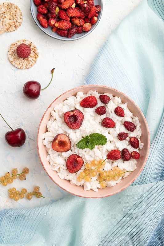Rice flakes porridge with milk and strawberry in ceramic bowl on white concrete background and blue linen textile. Top view, flat lay, close up