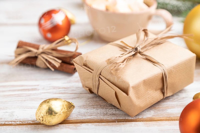 Christmas or New Year composition. Decorations, box, golden balls, cinnamon, fir and spruce branches, cup of coffee, on a white wooden background. Side view, close up, selective focus