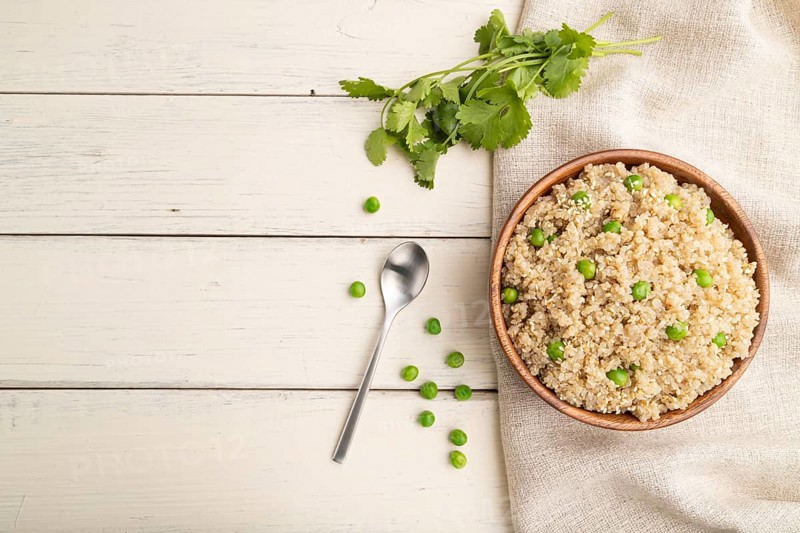 Quinoa porridge with green pea in wooden bowl on a white wooden background and linen textile. Top view, flat lay, copy space