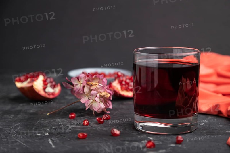 Glass of pomegranate juice on a black concrete background with red textile. Side view, close up, copy space