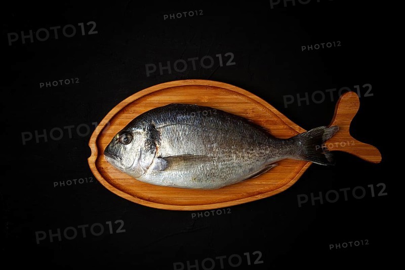 Raw fresh dorado fish, wooden plate in the shape of a fish, on a black table, top view, no people