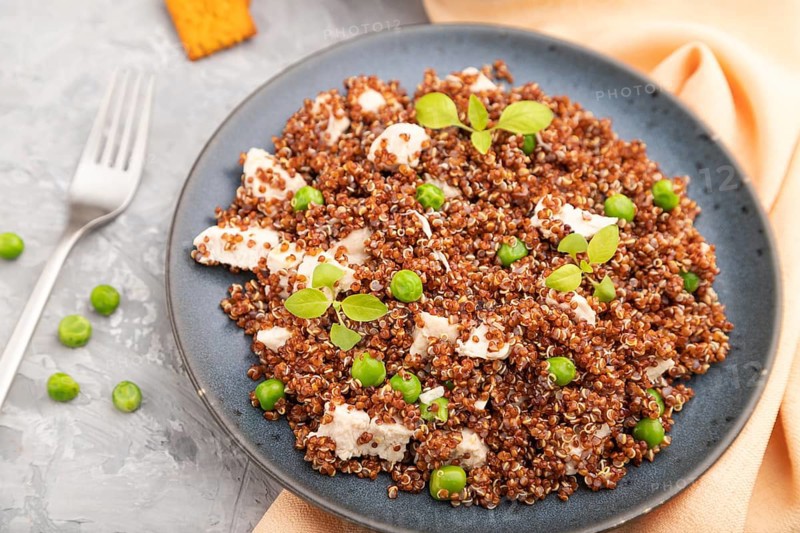 Quinoa porridge with green pea and chicken on ceramic plate on a gray concrete background and orange textile. Top view, close up, selective focus