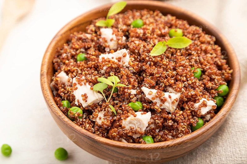 Quinoa porridge with green pea and chicken in wooden bowl on a white wooden background and linen textile. Side view, close up, selective focus