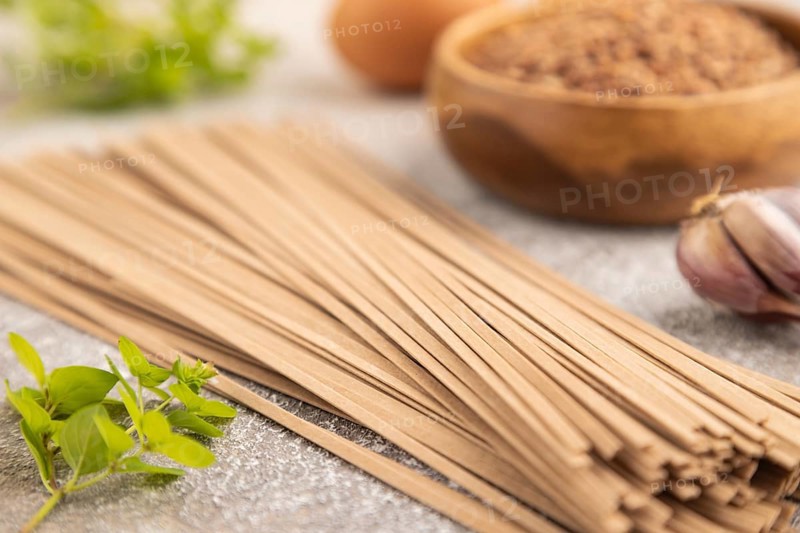 Japanese buckwheat soba noodles with tomato, eggs, spices, herbs on brown concrete background. Side view, close up, selective focus